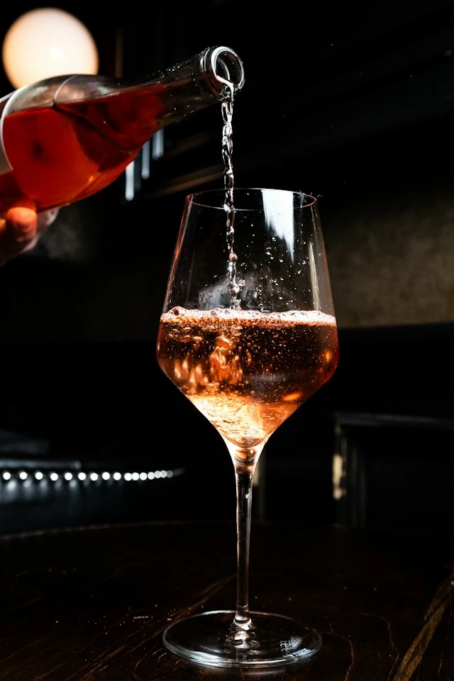 Champanhe rosa é derramado de uma garrafa em um copo grande